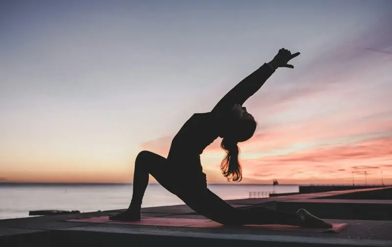 Mujer estirando junto al mar al atardecer